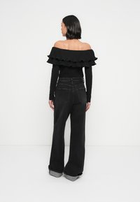 Must ülereva õlgadeta top volangidega, mis on kombineeritud kõrge vöökohaga tumedatest teksadest, millel on ülesrullitud sääred ja tavalised tagataskud.