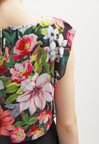 Blusa floral con fondo negro, que presenta flores vibrantes en tonos rosa, blanco y verde, fabricada en un tejido ligero y con un diseño relajado de manga corta.
