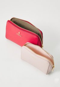 Two open Furla leather zip wallets, one red and one light pink, displayed on a white surface.