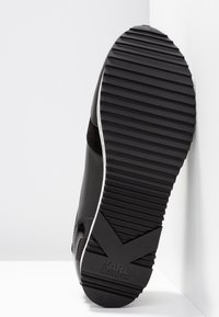 Semelle noire de basket avec de profondes rainures horizontales et le logo "KARL LAGERFELD" embossé près du talon.
