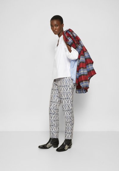 Camisa branca de manga longa, calças estampadas em azul e cinza, e sapatos pretos com detalhes em prata. Casaco xadrez vermelho e azul pousado sobre o ombro.