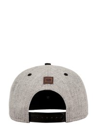 Pelēka auduma cepure ar platu maliņu, kurai ir melna snapback aizdare. Aizmugurē ir piestiprināta brūna ādas plāksne ar uzrakstu "MSTRDS MUNICH".