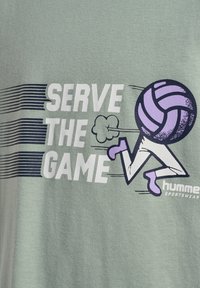 Grön bomullströja med en grafisk design som har texten "SERVE THE GAME" och en stiliserad volleybollspelare. Accenter i lila och marinblå.