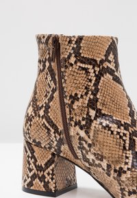 Botín de tobillo con estampado de serpiente marrón, detalle de cremallera en el costado, tacón cuadrado y superficie texturizada.