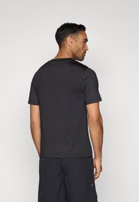 Juodas trumpų rankovių marškinėliai su apvalia iškirpte, glotnia tekstūra ir prigludusia forma. Atgalinis vaizdas atskleidžia paprastą, neišsiskiriantį stilių.