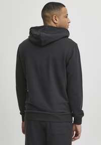 Black hoodie made of soft fabric, featuring a back neck hood, ribbed cuffs, and waistband, with a relaxed fit and minimal design.