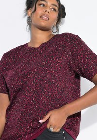 T-shirt con stampa leopardata in bordeaux e nero, maniche corte, scollo tondo, tessuto morbido, vestibilità rilassata, con dettaglio in ematite uniforme.