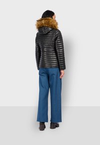 Černá péřová bunda s horizontálním prošíváním, odnímatelná hnědá kožešinová kapuce, spárované s širokými modrými džíny a masivními černými botami.