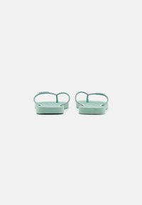 Des tongs vert clair avec une semelle texturée et de fines lanières. Les lanières présentent un léger éclat et un design minimaliste.