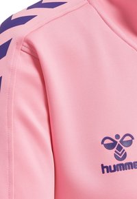 Pink stof med navy blå hummel-logo og chevron mønster på skuldersømmen af et sportstøj.