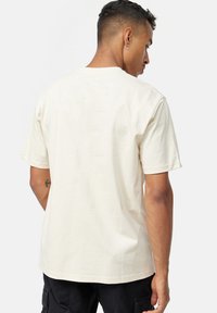Camiseta de algodón crema con mangas cortas, cuello redondo y un corte relajado. Textura suave con un detalle de costura mínimo en el dobladillo.