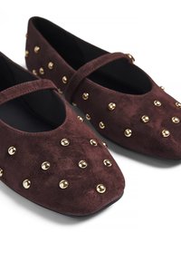 Ballerines en daim bordeaux à bout rond, avec une sangle décorative et des clous dorés répartis uniformément sur la surface supérieure.