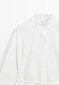 Witte blouse met een hoge kraag, voorzien van een knoopsluiting aan de voorkant en brede mouwen. Soepele textuur, minimalistisch design, zonder patronen of accenten.