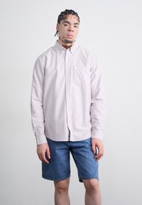 Chemise boutonnière rose clair à manches longues avec une poche poitrine, associée à un short en denim bleu. Tissu lisse et design classique.