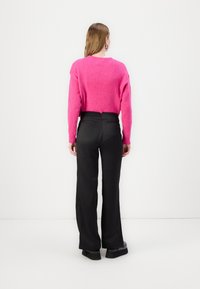 Φούξια βελούδινος πουλόβερ με μακριά μανίκια, συνδυασμένο με μαύρες παντελόνες φαρδιάς γραμμής. Απαλή υφή και εφαρμοστό μέσο με τσέπες στο πίσω μέρος.