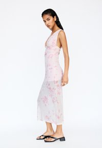 Genomskinlig rosa blommig klänning med en figurnära silhuett och djup urringning, i midi-längd och enkla svarta sandaler.
