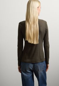 Langärmliges, olivgrünes, geripptes Oberteil, an den Schultern eng anliegend, mit abgerundetem Saum, kombiniert mit hellblauen, hoch taillierten Jeans.