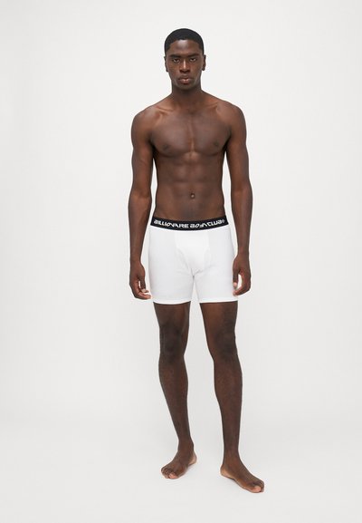 Boxers en coton blancs avec une ceinture de logo noire, présentant un design ajusté et une texture lisse, affichés sur une silhouette masculine.