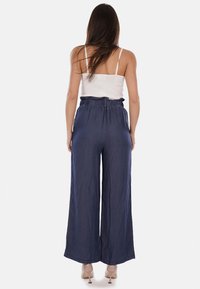 Pantaloni in denim a gamba larga con cintura elasticizzata, caratterizzati da una texture liscia e da un colore blu scuro. La vista posteriore mostra il fit rilassato e la forma.