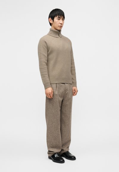 Μπεζ ριμπ πλεκτό πουλόβερ με ρολό λαιμό και διπλωμένο γιακά, συνδυασμένο με φαρδιά ανοιχτό καφέ μάλλινα παντελόνια και μαύρα δερμάτινα παπούτσια.