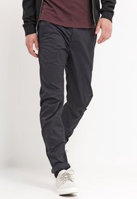 Mörkblå chinos med en slät tygstruktur, skräddarsydd passform och sidofickor. Matchas med ljusgrå sneakers och en mörk zip-up jacka.