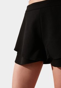 Černé sportovní šortky s vrstvenou sukní, vyrobené z hladkého materiálu, s vysokým pasem a volným střihem kolem stehen.