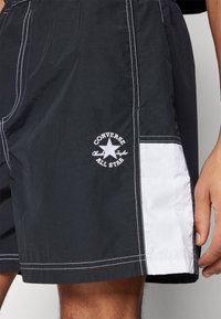 Černé plavky s bílými akcenty. Materiál je lehký, s vyšitým logem Converse a kontrastním švem.