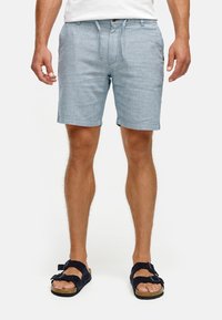 Lichtblauwe chambray shorts met een trekkoord in de taille, zijzakken en opgerolde zomen. Draagmode met zwarte sandalen met dubbele bandjes.