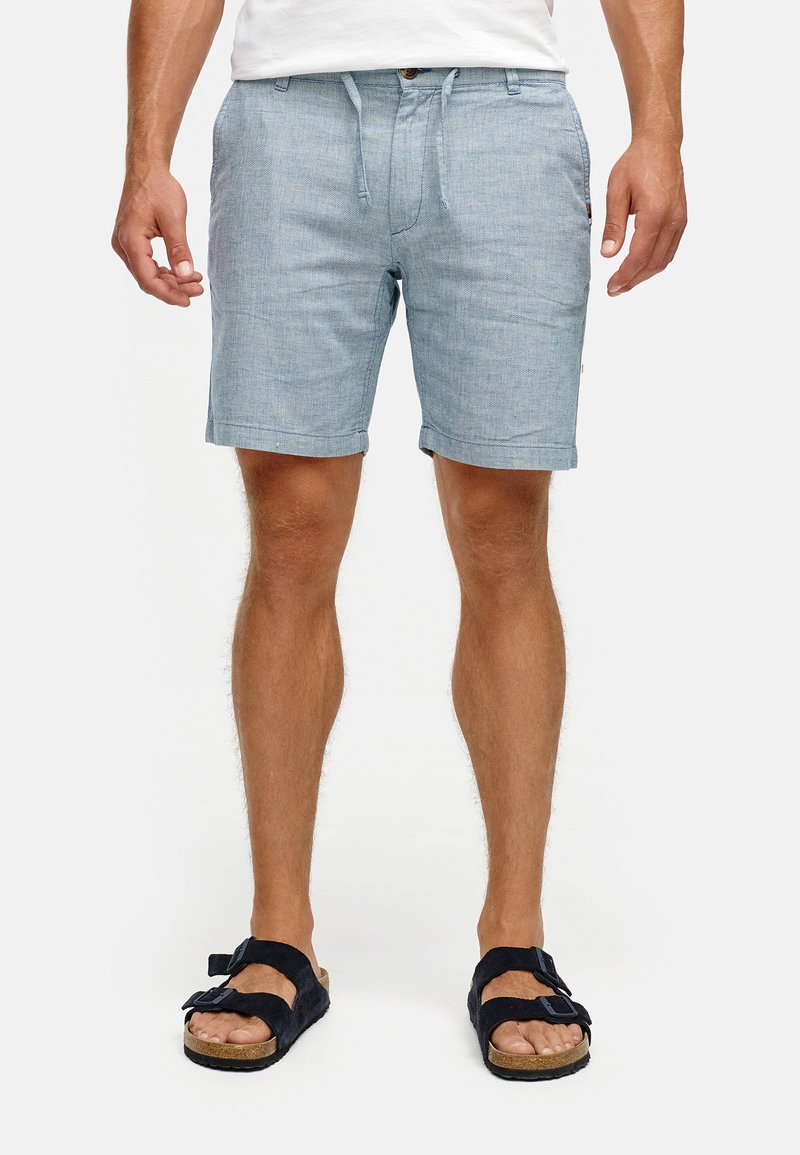 Lichtblauwe chambray shorts met een trekkoord in de taille, zijzakken en opgerolde zomen. Draagmode met zwarte sandalen met dubbele bandjes.