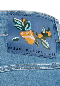 Denimstoff mit einem blauen Etikett, das florale Stickerei in Orange und Grün aufweist, der Text lautet "DREAM WONDERLIGHT" in Schwarz.