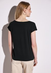 T-shirt nera a maniche corte con scollatura ampia, texture liscia e vestibilità rilassata. Progettata con spacchi ai lati per un maggiore comfort.