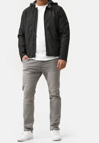 Mustat nahkatakki hupulla, teksturoitu olkapäät, vetoketjukiinnitys edessä, yhdistetty vaaleanharmaisiin housuihin ja valkoisiin tennareihin.