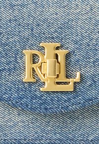 Guldtonad metallogo "RL" som är tydligt visad på en strukturerad blå denimbakgrund. Logotypen har en låsdesign med en polerad finish.