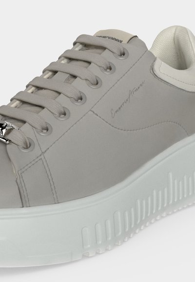 Ανοιχτό γκρι sneaker χαμηλού τύπου με χοντρή λευκή σόλα, γκρι κορδόνια και διακριτικό λογότυπο "Emporio Armani" στην πλαϊνή πλευρά και στη γλώσσα.