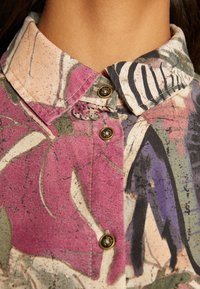 Camicia con colletto abbottonata; presenta un motivo floreale multicolore in rosa, viola, verde e nero; include bottoni in ottone.