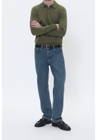 Polo verde a maglia con due bottoni, abbinata a jeans di denim blu, cintura nera e scarpe nere in pelle verniciata con lacci.