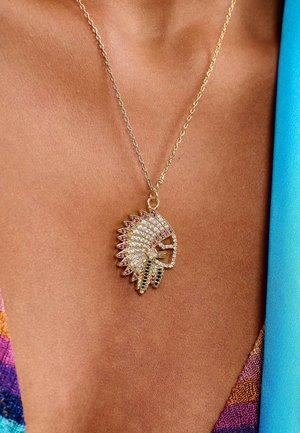 Collier en chaîne dorée présentant un pendentif détaillé et étincelant en forme de coiffe de chef, orné de pierres précieuses transparentes et violettes.