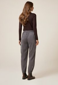 Pantalones de pana grises con un corte relajado, cinturilla elástica y puños ajustados, combinados con una camiseta de manga larga marrón y botas negras de tobillo.