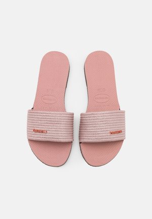 Par lyserøde Havaianas slip-sandaler med teksturerede fodsenge og ribbet stofremme, der har orange brandlogos på remmene.