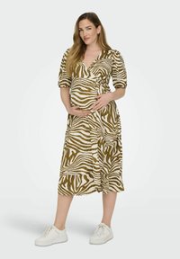 Korte mouwen, wikkeljurk met een bruin en crèmekleurig zebrapatroon, taillering bij de taille, gecombineerd met witte sneakers. Middellange, lichte stof.