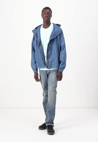 Jeansjakke i lyseblå, med lange ermer og hette. Kombinert med en mintgrønn t-skjorte og falmede blå jeans. Svarte sko.