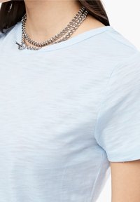 Vaaleansininen puuvillapaita, jossa on pehmeä tekstuuri, pyöreä kaula-aukko ja lyhyet hihat; sisältää kerrosmainen hopeaketjuista.