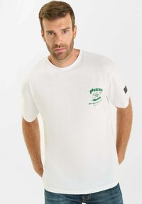 Witte katoenen t-shirt met korte mouwen en een ronde hals. Voorzien van een groene grafische print op de linkerborst en een zwart accent op de mouw.