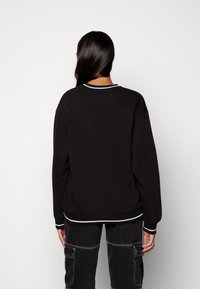 Svart sweatshirt med rund halsringning, vitrandig ribbad kant vid krage och ärmslut, samt en avslappnad passform. Texturerad tyg och enkel design.