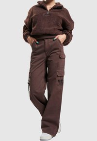 Brun fleece-pullover med halv dragkedja och avslappnad passform, i kombination med bruna cargo-byxor med stora sidofickor och logodetalj.