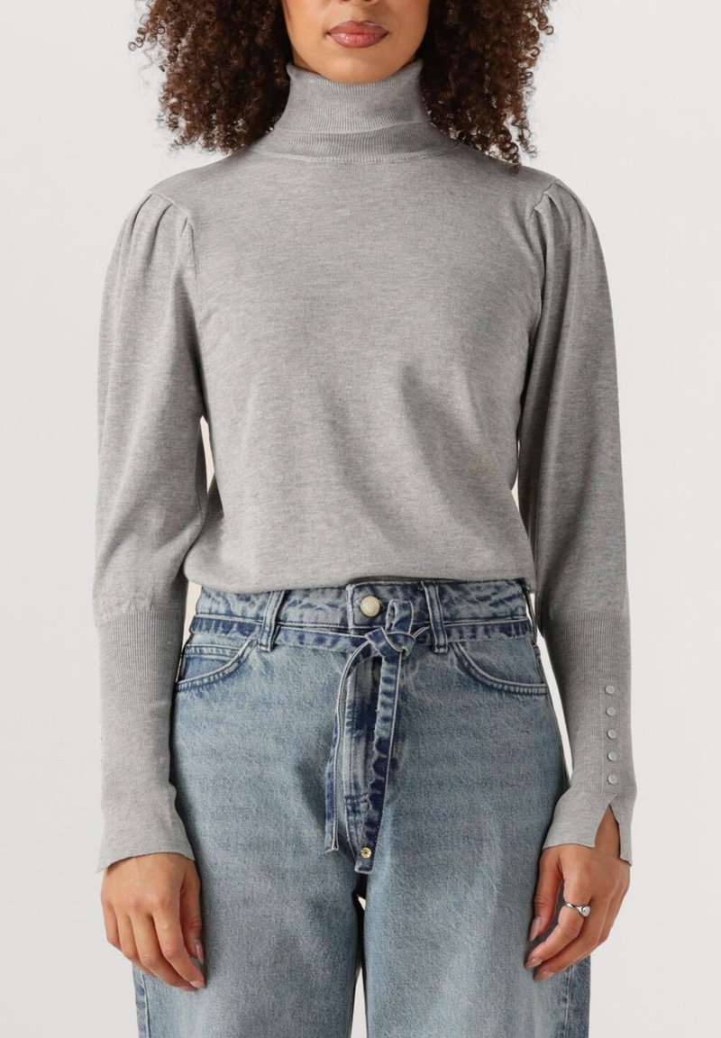 Grauer gestrickter Rollkragenpullover mit Puffärmeln und Knopfdetails, kombiniert mit hoch-taillierten hellblauen Jeans. Texturiertes Gewebe und entspannter Schnitt.