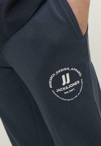 Pantalones jogger en azul marino hechos de suave algodón, con un logo blanco redondo en el muslo izquierdo, que presenta el texto "JACK & JONES" y acentos.