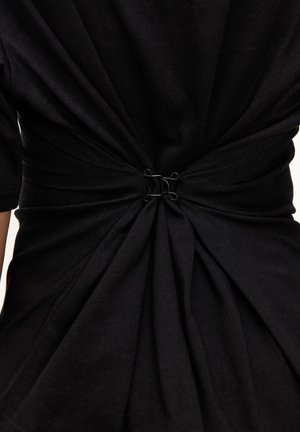 Tissu noir rassemblé et serré à la taille avec deux petites agrafes métalliques à crochet, créant des plis et de la texture.