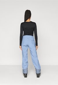 Μπλε παντελόνι χιονιού με ίσια εφαρμογή, ελαστική μέση και μανίκια με αντίθεση σχεδίου. Φορεμένο με μαύρο μακρυμάνικο τοπ και μαύρες μπότες.