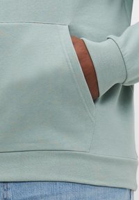 Lichtblauwe hoodie met een kangoeroezak, ribgebreide manchetten en zoom. Zachte textuur en casual ontwerp zichtbaar in close-up.
